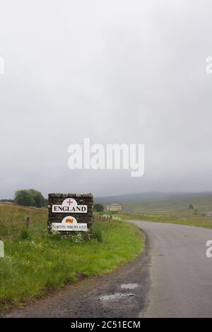 Pilastro di pietra e segni che segnano il confine tra Inghilterra e Scozia vicino su una strada non classificata a Deadwater, Kielder, Northumberland in una giornata noiosa e nebbiosa. Foto Stock