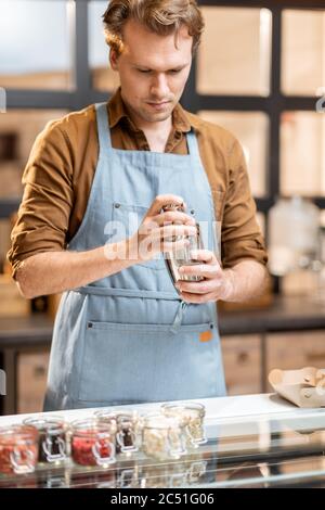 Venditore che mescola diversi condimenti per il gelato per spruzzare sul gelato al cioccolato presso il negozio, primo piano Foto Stock