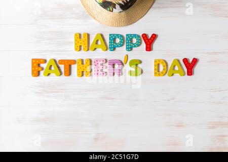 Happy Father's Day iscrizione di lettere colorate in legno e cappello estivo su sfondo di legno d'epoca. Frase Felice Padri giorno e cappello su legno bianco ba Foto Stock