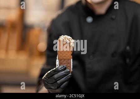 Chef in uniforme nera con gelato al cioccolato, primo piano Foto Stock