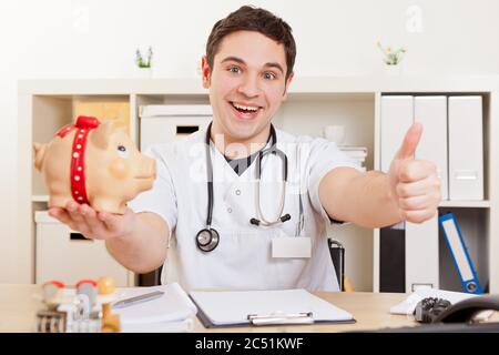 Ridendo medico con la banca piggy in ufficio tiene il pollice in su Foto Stock