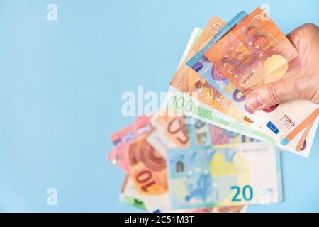 Persona che tiene a mano banconote in euro e altre banconote sfocate su sfondo blu. Mano con banconote europee isolate su sfondo azzurro. Euro in contanti Foto Stock
