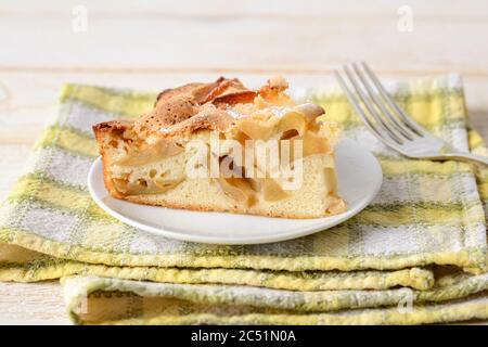 Un pezzo grande di torta di mele dolce e acide su un piatto bianco su un tovagliolo giallo-verde a scacchi. Ricetta per dolci e dolci fatti in casa. Pasticceria per la colazione. Foto Stock
