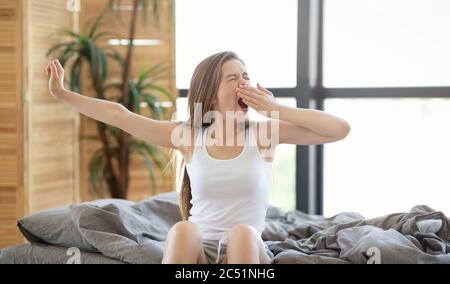 Donna sonnolenta che urla e si stende sul suo letto dopo essersi svegliata, in interni Foto Stock