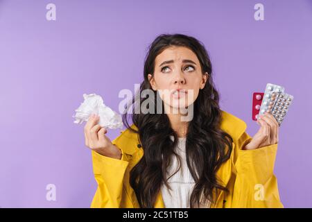 Immagine di triste pensare malata donna isolato su sfondo viola parete tenendo tovagliolo e pillole medicina. Foto Stock