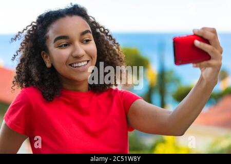 Bella biracial misto razza Africano americano adolescente ragazza giovane donna sorridente con denti perfetti prendendo selfie cellulare fuori dal mare Foto Stock