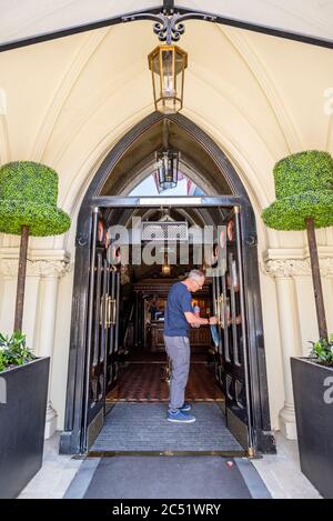 Ian, uno dei dirigenti, pulisce le maniglie delle porte anteriori del Randolph Hotel, Oxford, pronto per riaprire dopo il blocco Covid-19 il 4 luglio 2020 Foto Stock