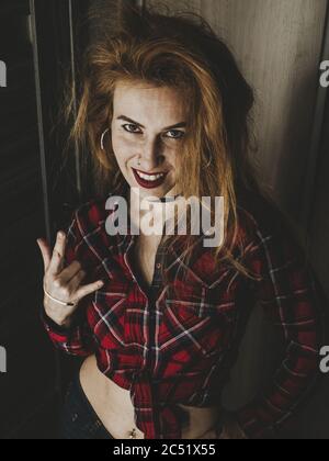 Ragazza con frugoso sorriso divertente hairdo e mostra gesto per rock Foto Stock