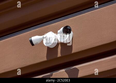 Due telecamere TVCC bianche installate sulla facciata esterna di una parete marrone, primi piano sistemi di sorveglianza e controllo remoto degli ordini in giornata di sole. Foto Stock