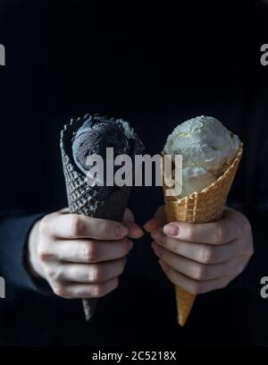 Gelato nero e gelato bianco in una tazza di waffle a mani femminili. Cibo alla moda. Spazio di copia Foto Stock
