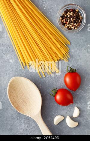 Spaghetti crudi con pomodori, aglio, pepe e cucchiaio di legno su fondo grigio. Vista dall'alto. Foto Stock