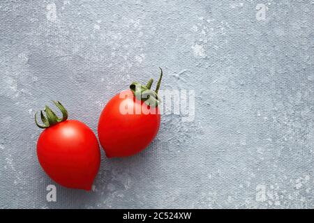 Due pomodori ciliegini freschi su fondo grigio con spazio per la copia. Vista dall'alto. Foto Stock