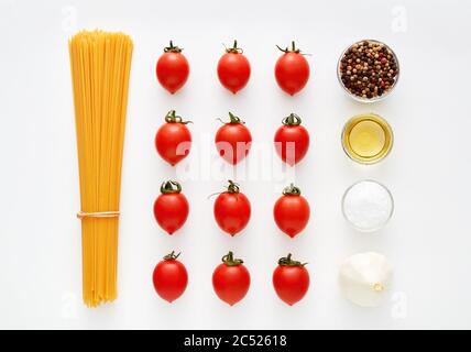 Spaghetti crudi con pomodori, aglio, pepe, sale e olio d'oliva su fondo bianco. Preparazione della pasta e ricetta della salsa. Foto Stock