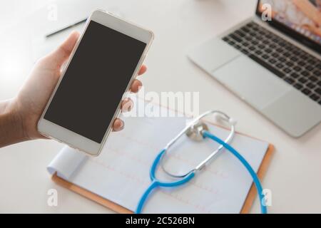 Medico che usa il telefono cellulare che legge rapporto trattamento su desk.healthcare e concetto di tecnologia. Foto Stock