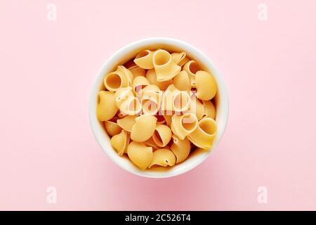 Un mucchio di pasta rigata pipettata in un recipiente bianco su sfondo rosa. Vista dall'alto. Foto Stock