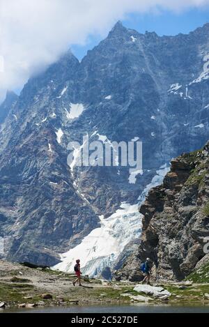 Breuil-Cervinia, Italia - 23 luglio 2019: Due viaggiatori con zaini percorso escursionistico collinare con collina rocciosa sullo sfondo. Donna e uomo che godono di vista della cresta rocciosa picco mentre escursioni in montagna Foto Stock