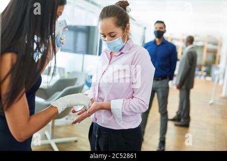 Donna d'affari che disinfetta le mani di un collega davanti all'ufficio come prevenzione per Covid-19 Foto Stock