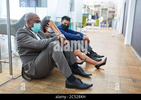 La gente triste di affari con la maschera di faccia siede sul pavimento dell'ufficio dopo il sacking o il lavoro di breve tempo Foto Stock