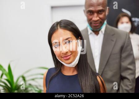 Giovane donna d'affari attraente con maschera sul mento insieme con la collega Foto Stock