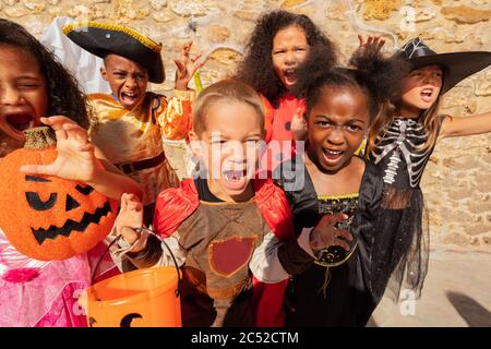 Molti bambini gridano e guardano la macchina fotografica in costumi di Halloween che si levano insieme in un gruppo di amici Foto Stock