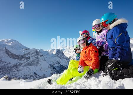 Un grande gruppo di bambini si siede sul mucchio di neve sulle cime della catena montuosa in un colorato vestito sportivo Foto Stock