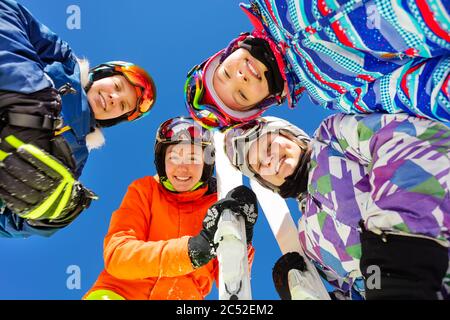 Gruppo di bambini in sci in maschera sport maschera e caschi si affacciano insieme in piedi su cielo blu Foto Stock