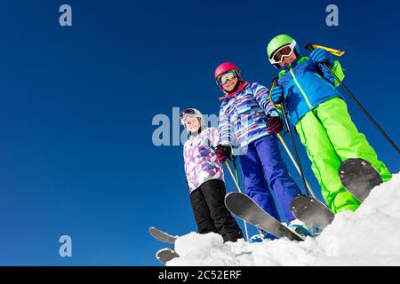 Vista dal basso di un gruppo di tre bambini in cima alla montagna con un vestito da sci colorato sulla neve, sopra il cielo blu Foto Stock