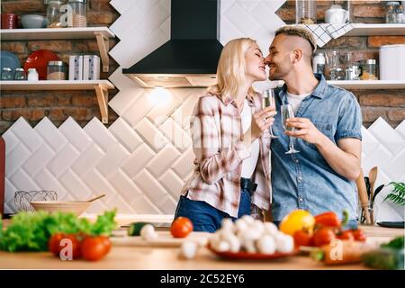 Giovane coppia felice bevendo champagne e godendosi la compagnia l'una dell'altra in cucina a casa. Relazione, concetto di celebrazione Foto Stock