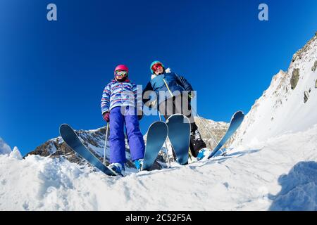 Vista dal basso di due ragazze che si ergono su sci indossando caschi e maschere sulla cima della montagna Foto Stock