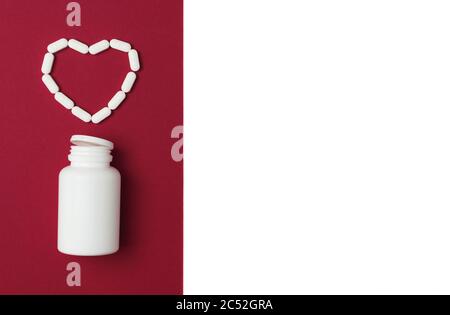 Bottiglia mock-up con pillole bianche versate a forma di cuore su sfondo rosso e bianco isolato. Stile di posa piatto. Spazio di copia. Medicina, sanità e concetto di farmacia. Foto Stock