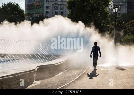 Piazza Unirii, Bucarest, Romania. Come parte delle spettacolari fontane, un appannamento di acqua sistema raffredda i passanti durante il soffocante calore estivo Foto Stock