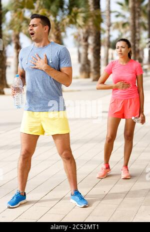 Coppia di fitness stanca che prende la pausa e beve acqua fredda dopo un allenamento all'aperto difficile Foto Stock