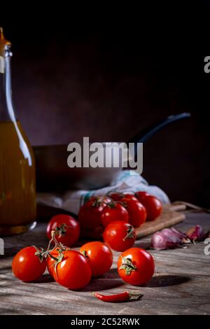 Pomodori ciliegini su tavolo di legno vecchio con aglio, peperoncino e olio d'oliva Foto Stock