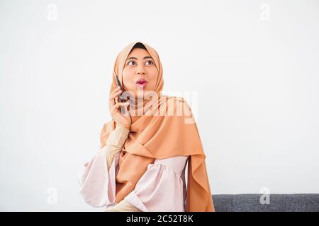 Felice giovane musulmana seduta sul divano prendere ritratto con il telefono a casa. Felice donna araba in hijab con telefono cellulare facendo selfie. Foto Stock