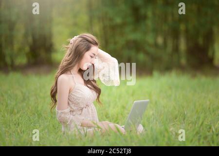Donna seduta in un campo che lavora sul suo laptop, Thailandia Foto Stock