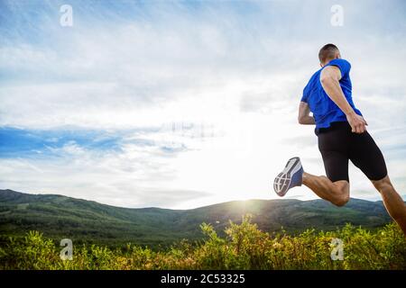 indietro atleta corridore correre prato di montagna in raggi di tramonto Foto Stock