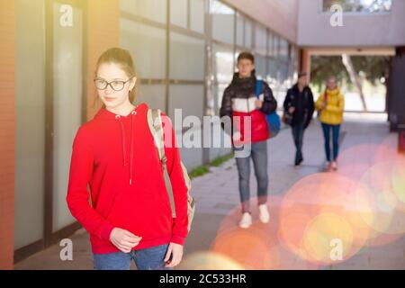 Ragazza adolescente sorridente con cappuccio rosso che cammina al campus universitario il giorno della primavera Foto Stock