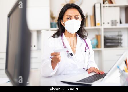 Terapista latino-americano sicuro che indossa una maschera protettiva che fornisce prescrizioni al paziente dopo la consultazione in ufficio medico Foto Stock