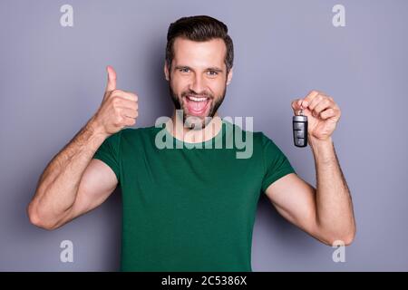 Ritratto di eccitato positivo ragazzo auto acquirente tenere chiavi godere eccellente acquisto mostra pollice su segno indossare t-shirt verde isolato su colore grigio Foto Stock