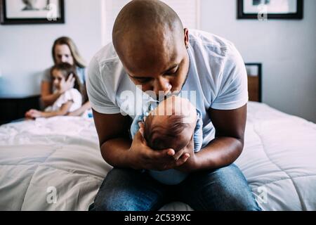 papà baciando il neonato a letto con mamma e figlia dentro massa posteriore Foto Stock