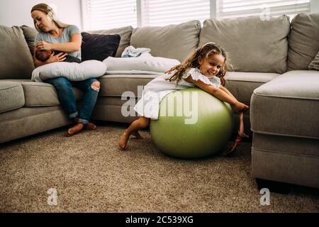 giovane ragazza che gioca mentre la madre tiene il nuovo bambino Foto Stock