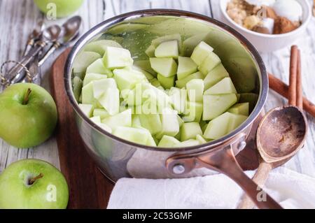 Ingredienti di mele verdi Granny Smith a dadini freschi in una padella con ingredienti che si trovano vicino per preparare torte di mele o torte. Messa a fuoco selettiva con Foto Stock