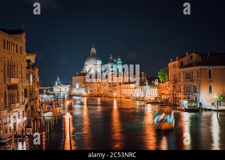 Venezia, Italia. Canal Grande di notte. Luce di illuminazione riflessa sulla superficie dell'acqua. Maestosa Basilica di Santa Maria della Salute sullo sfondo. Foto Stock