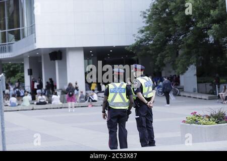Due ufficiali di polizia osservano da lontano mentre la gente si riunisce per una protesta pacifica contro il razzismo di BLM al Municipio di Hamilton, Ontario Canada Foto Stock