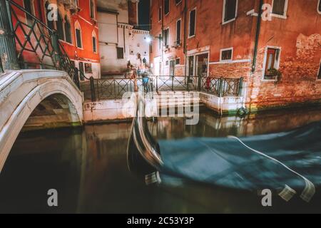 Venezia Gondola in piccolo canale con ponte ad arco nella città lagunare Venezia di notte. Lunga esposizione Venezia Italia. Foto Stock