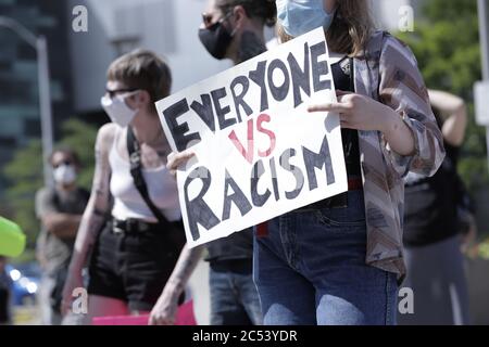 Una giovane donna ha visto tenere un cartello dicendo tutti contro il razzismo, durante una protesta Black Lives materia al Municipio di Hamilton Foto Stock