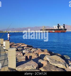 EILAT, ISRAELE - 31 MARZO 2015: Pescatore nel porto di Eilat, nave Genmar Vision ormeggiata in background durante il tramonto, Israele Foto Stock