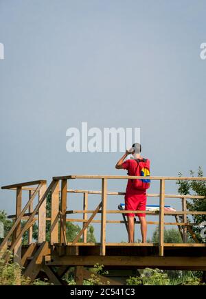 Uomo che guarda gli uccelli attraverso un binocolo da un posto di osservazione birdwatching nella Riserva Naturale del Parco Vacaresti. Foto Stock