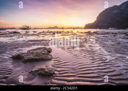Corong Spiaggia, El Nido, Filippine. Tramonto sulla spiaggia tropicale. Sole riflessioni all'ora d'oro. Catena di montagna isole all'orizzonte. Foto Stock