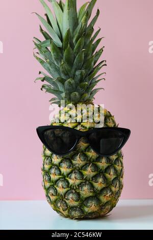 pazzo ananas con occhiali da sole davanti a uno sfondo rosa, concetto per l'estate o la vacanza Foto Stock